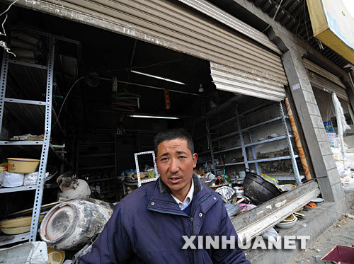 在拉萨市藏热南路，从青海来拉萨做生意的马么乃站在他被不法分子损毁的小店前（3月16日摄）。     