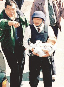 邱丰光(左)担任台北市刑大副大队长时,在南非武官的官邸围捕白晓燕案嫌犯陈进兴,陪同当时大队长侯友宜(右)救出一名婴儿,邱丰光稍后再勒押着陈进兴走出现场。 图片来源:台湾《联合报》