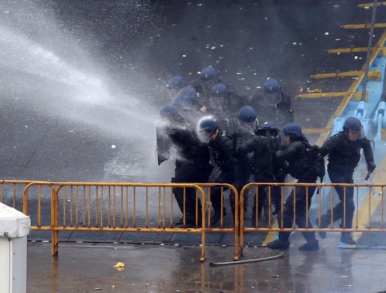 图为多位警察用盾牌缓解水龙的冲击