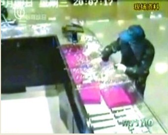 劫匪将柜台里的金饰品装入袋子
