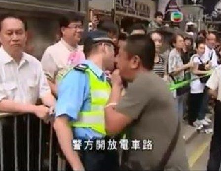 由电视台的片段中，可见被告纪镇基（灰衣者）去年一场游行期间走近辅警，在其耳边吹口哨。（无线电视画面）